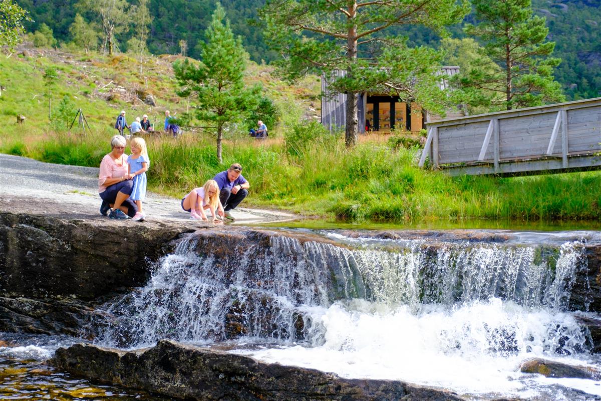 Familie leker i elv i naturlandskap - Klikk for stort bilde